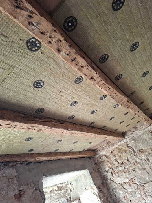 Rengjorda takbjälkar med monterad stenull i ett sovrum under renovering.