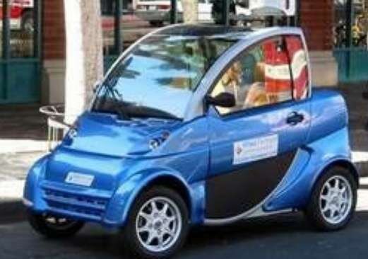 En liten blå elbil från mitten av 00-talet parkerad på en gata, med design som signalerar det tidiga stadiet av elfordon.