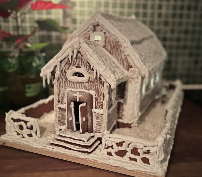Pepparkakshus som liknar Dalarö kyrka, dekorerat med vit glasyr och omgiven av ett staket.