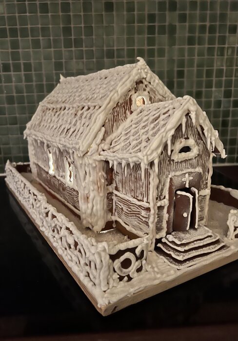 Pepparkakshus som föreställer Dalarö kyrka, dekorerat med rikligt kristyr, placerat på en bricka framför en grön kakelvägg.