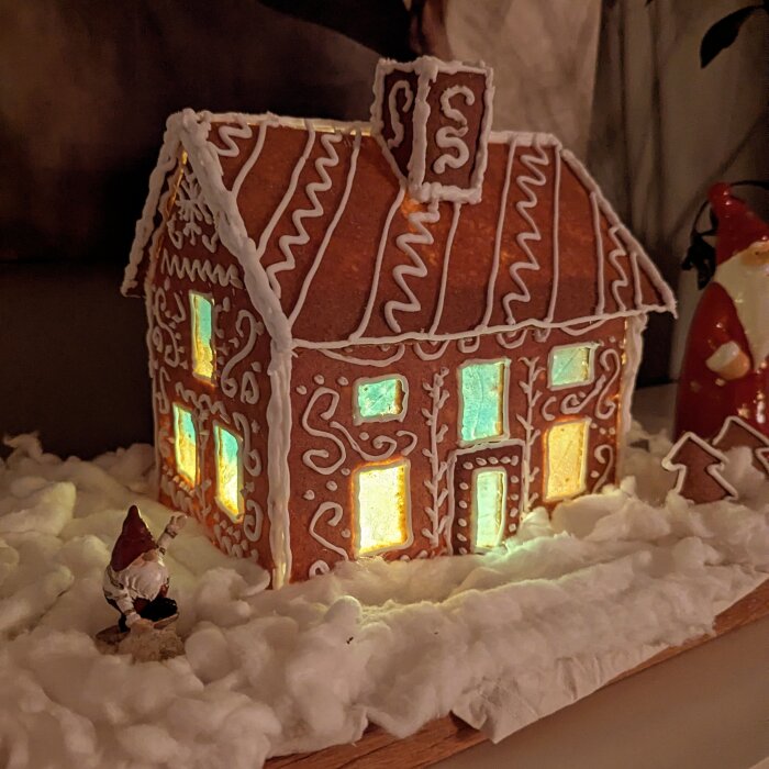 Pepparkakshus dekorerat som en nattklubb för tomtar med lysande fönster och snöprydd bas, bredvid står en liten tomtefigur.