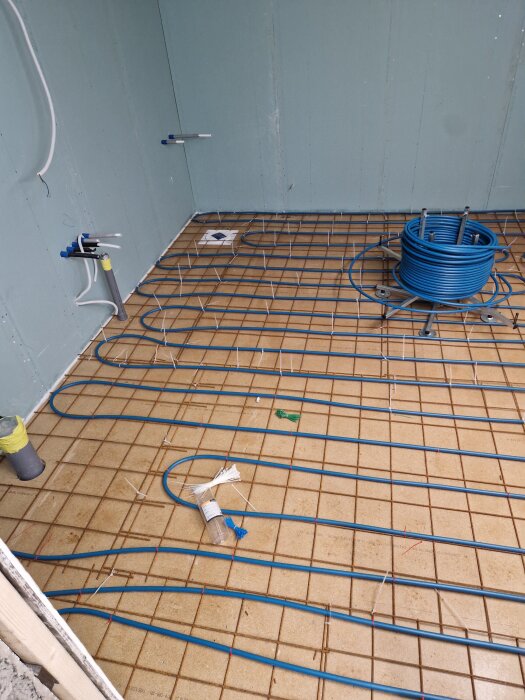 Elektriska kablar installerade på ett badrumsgolv med klinkerplattor och inslagna väggar för ett golvvärmesystem i ett renoveringsprojekt.