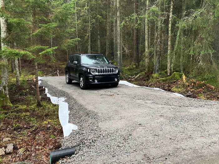 En nyanlagd grusinfart i skogen med en svart SUV parkerad på den. Kanten ser brant ut och är täckt av vit duk.