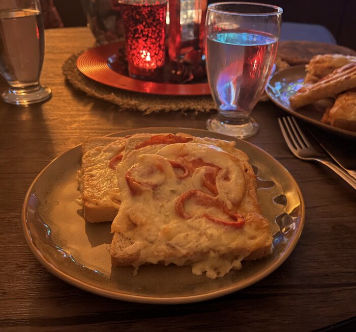 Varma mackor med paprikasalami, skinka, lök, tomat, paprika, ost och kryddor på tallrik med dryck i bakgrunden.