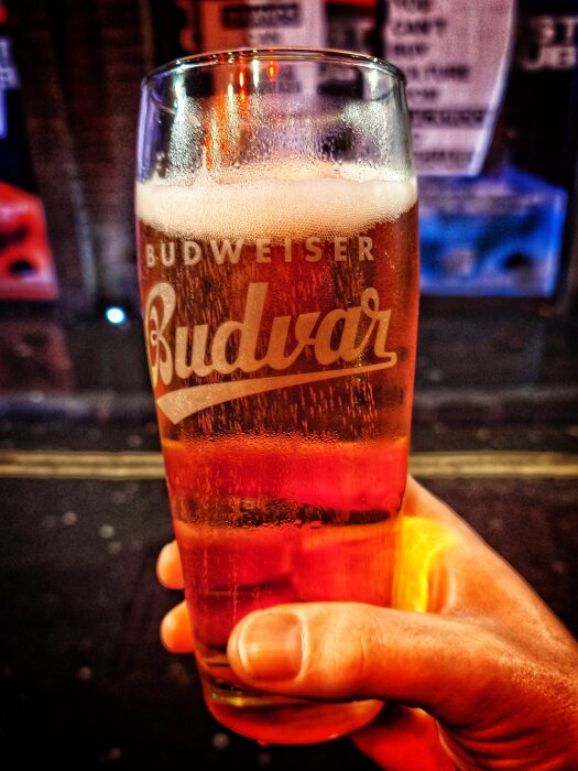 Ett glas Budweiser-hambärs hålls i en hand på en pub, eventuellt vid Bradleys Spanish Bar i London.