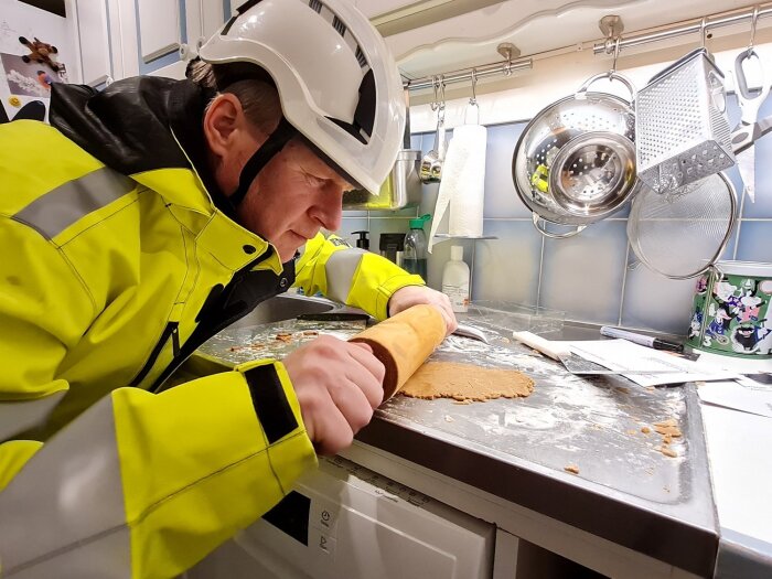 Byggnadsarbetare i hjälm och skyddskläder kavlar deg på en köksbänk, omgivet av köksredskap.