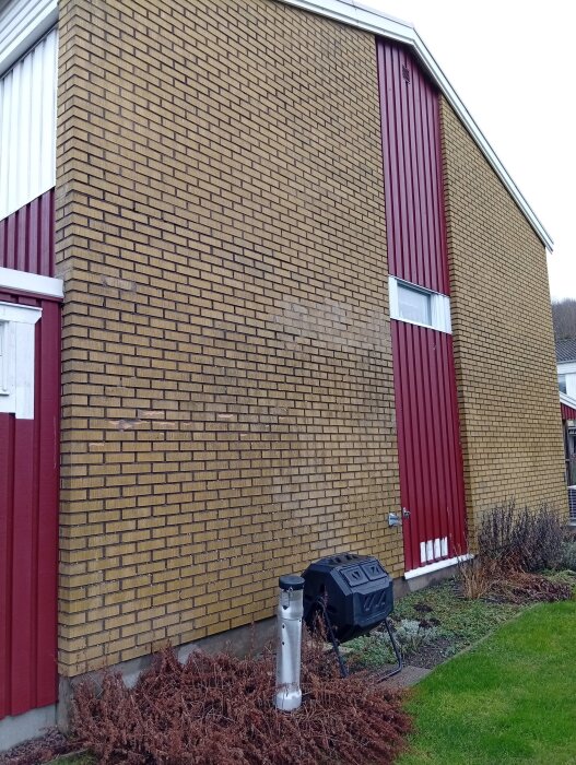 Tegelvägg på ett radhus från 70-talet med tecken på vittring och sprickor, bredvid en röd träpanel.