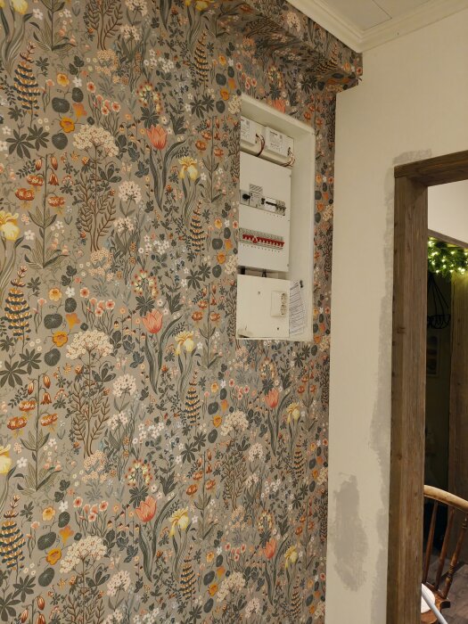 Blommig tapet med öppnat elskåp syns i ett kök vid sidan av en dörr.