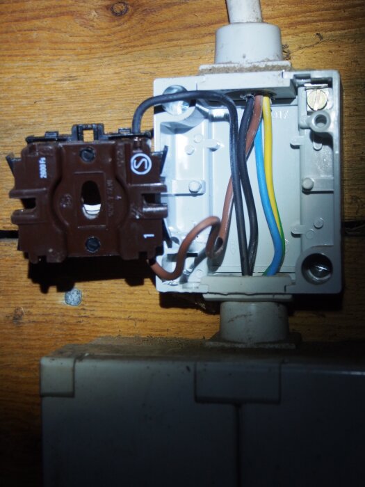 En öppnad kopplingsdosa med synliga elkablar och en brun strömbrytare mot en träbakgrund.