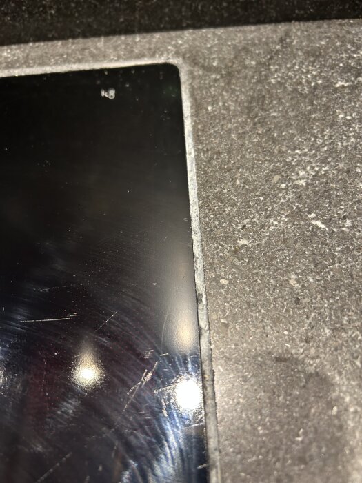 Tätning med svart silikon runt glas häll, monterad i laserskuret hål i stenskiva. Silikonen ser sliten ut.