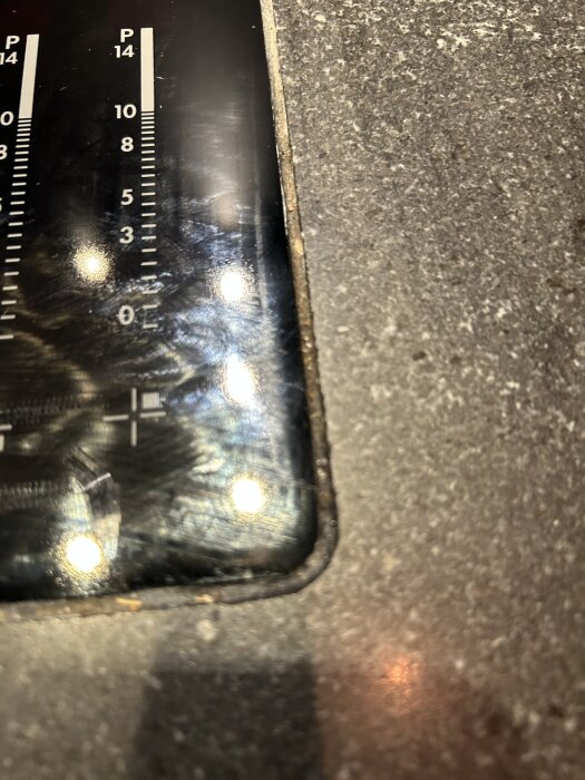 Närbild av en inbyggd häll med slitna svarta silikonkanter mot en stenskiva. Markeringar för temperatur eller styrka syns på hällen.