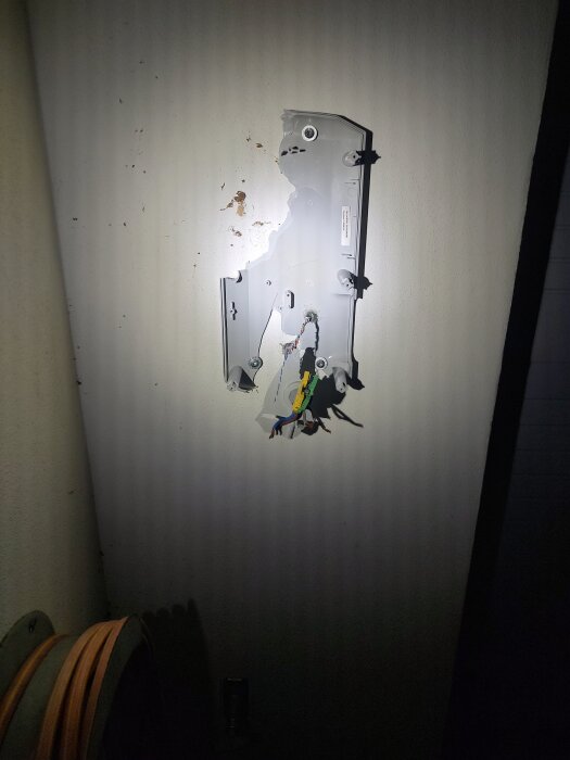 Skadad vägg med blottlagda elkablar och trasig apparatdosa monterad, belyst i mörker.