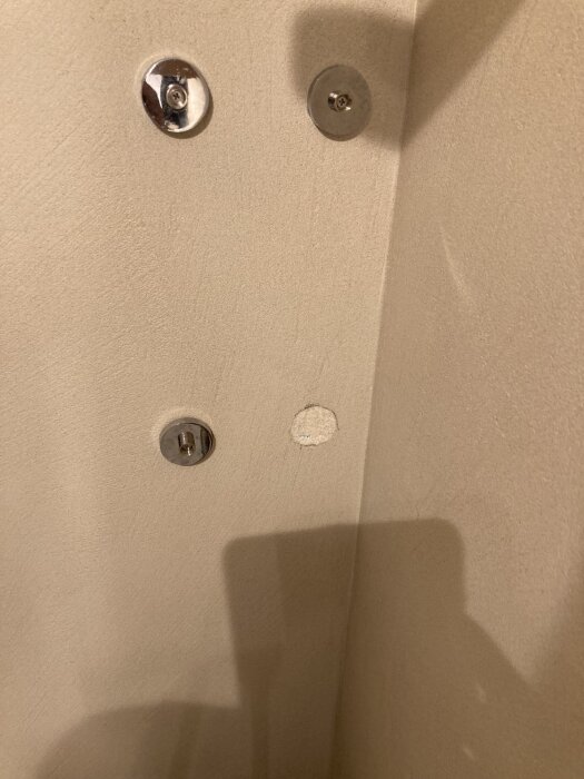 Hål i mikrocementvägg där hållare lossnat, med två fästen kvar och limrester synliga.