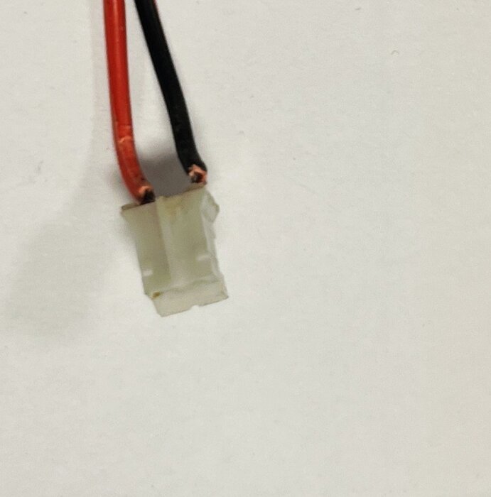 En vit elektrisk kontakt med två kablar, en röd och en svart, mot en vit bakgrund.