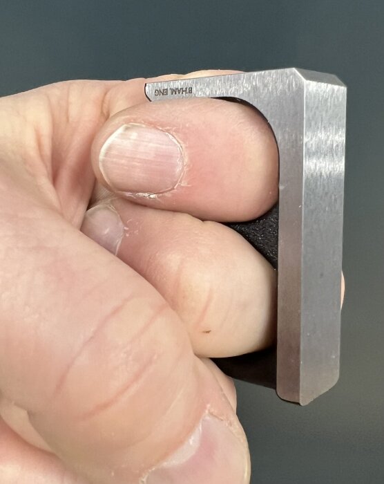 En hand som håller i en metalldel av ett verktyg, troligen ett knogjärn för användning i snickeri.