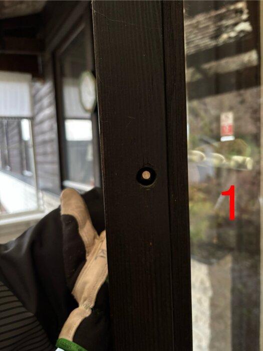 Altandörr med ett hål för handtag; hand i handske visar springan där en näbbtång kan användas för att vrida upp handtaget utifrån.