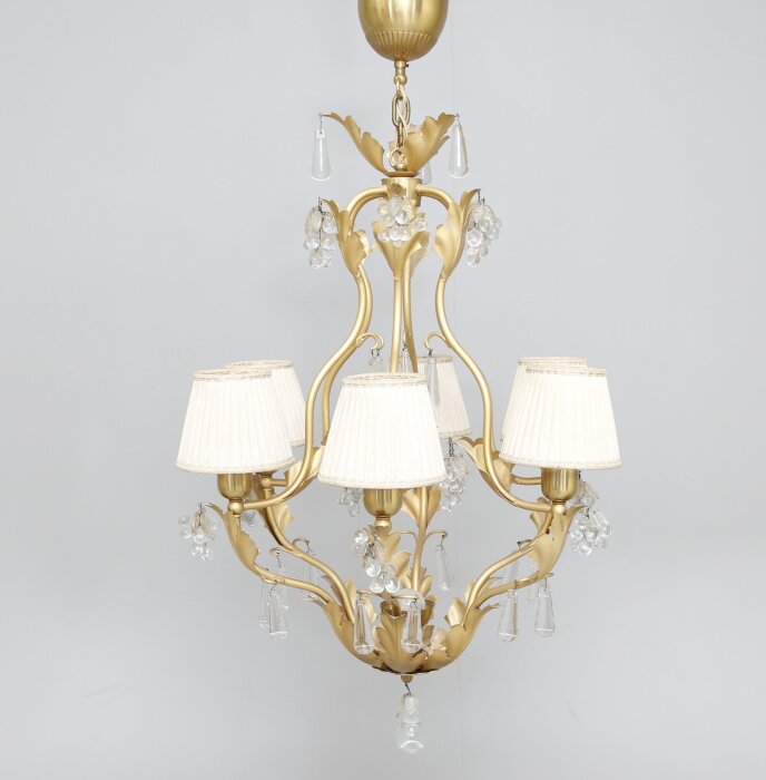 Elegant guldkrona med fem lampskärmar i vitt tyg och dekorativa prismor.