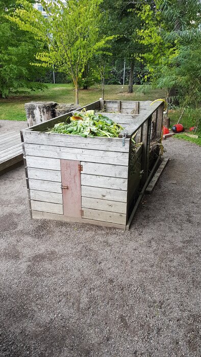 Träkompost med flera fack fylld med löv och växtrester, inspirerad av en konstruktion i Uppsala botaniska trädgård.