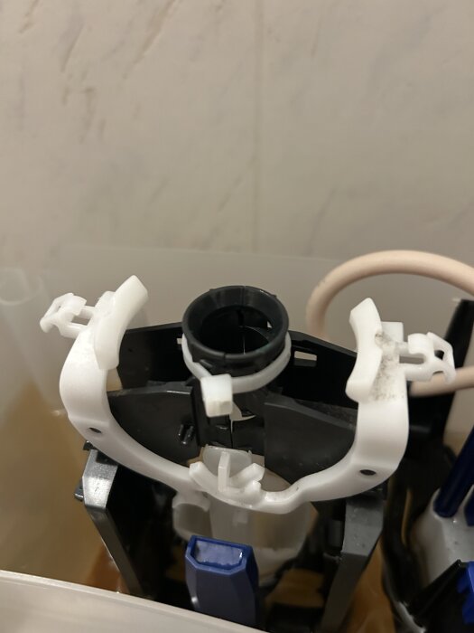 Trasigt toalettcisternelement utan kåpa med avbrutet plaströr som har reparerats med ett buntband för att återställa funktionen.