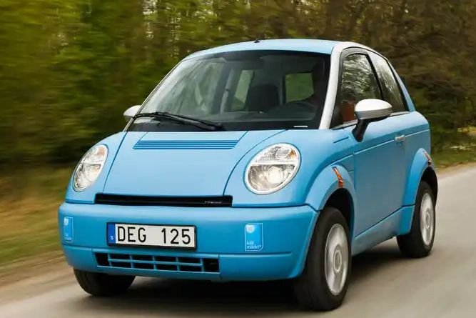 Blå elbil av märket som omnämns i inlägget, körandes på en landsväg med träd i bakgrunden.