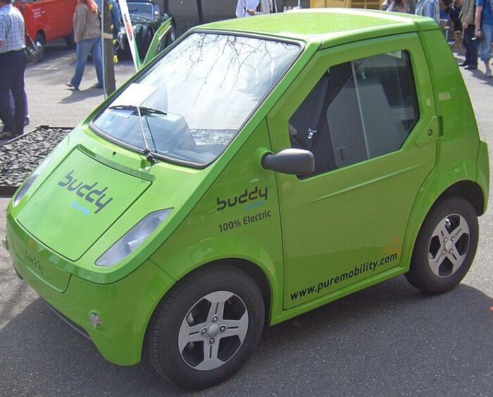 Grön elbil av märket Buddy, parkerad på en gata.