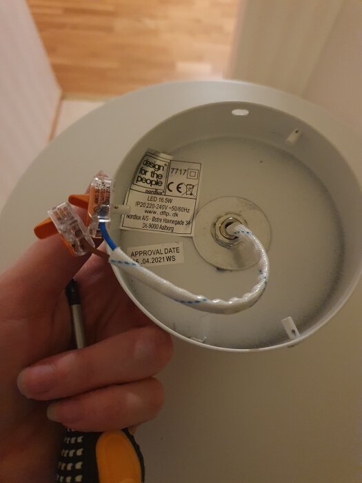 En person håller upp en lampbas med synliga elektriska kopplingar och ledningar i anslutning till en etikett.