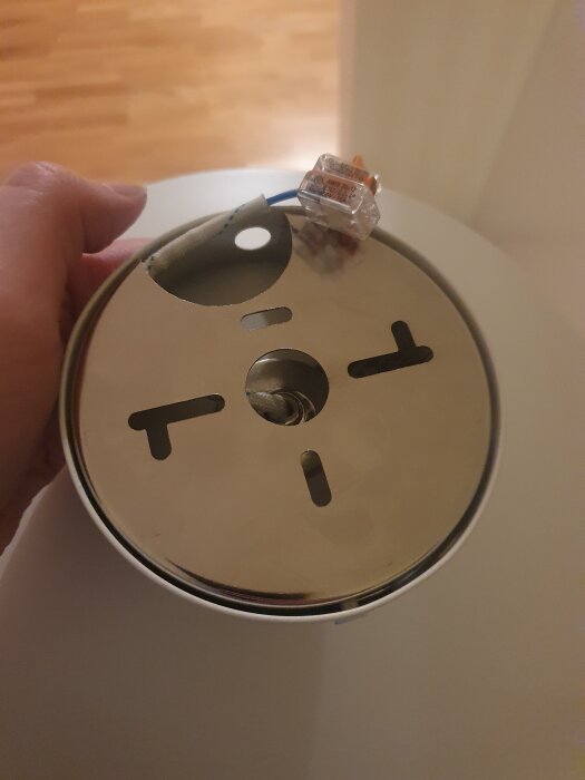 Hand håller en metallplatta med hål och elektriska trådar anslutna till en kopplingsklämma.