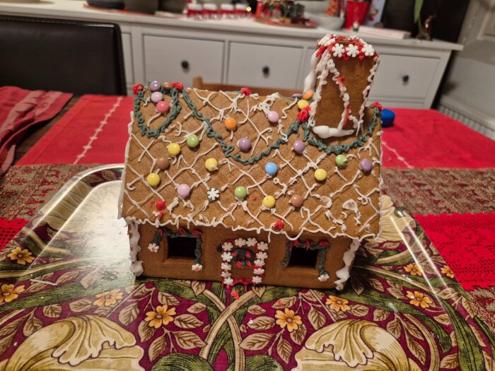 Dekorerat pepparkakshus med färgglada godisar och glasyr på rött bord; sällskap byggde huset utan brännskador, hälften av godiset kvar.