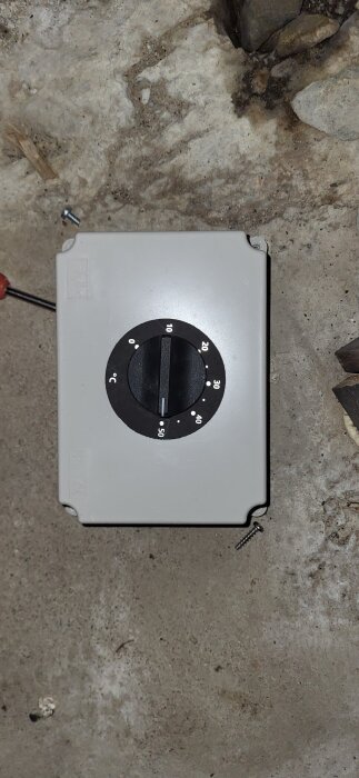 Termostat vridtermostat monterad på vägg med inställning i grader Celsius, synlig markering runt 40°C, på betonggolv med skruvar bredvid.