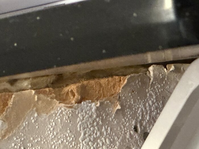 Närbild av skadad mur eller puts under bänkskiva med sprucken och flagnande yta.