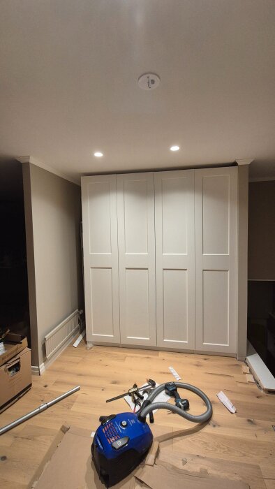 Inbyggda vita garderober i hallen med verktyg och en dammsugare på golvet, interiörbild under renovering.