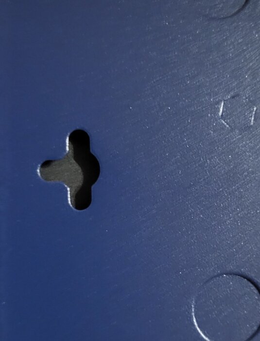 Anslutningshål med slits på en blå plastyta, för skruvupphängning av objekt såsom en switch.