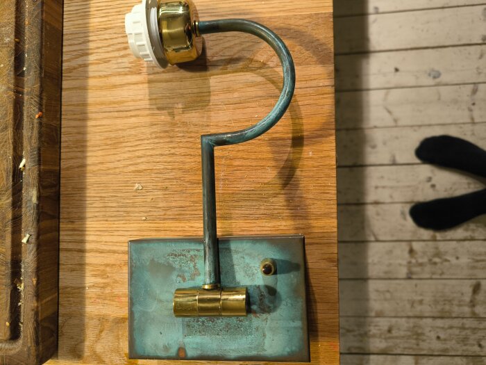 Gammal lamparmatur i mässing och patinerad metall på träbord med elsockel, diskussion om att byta till LED-lampa.