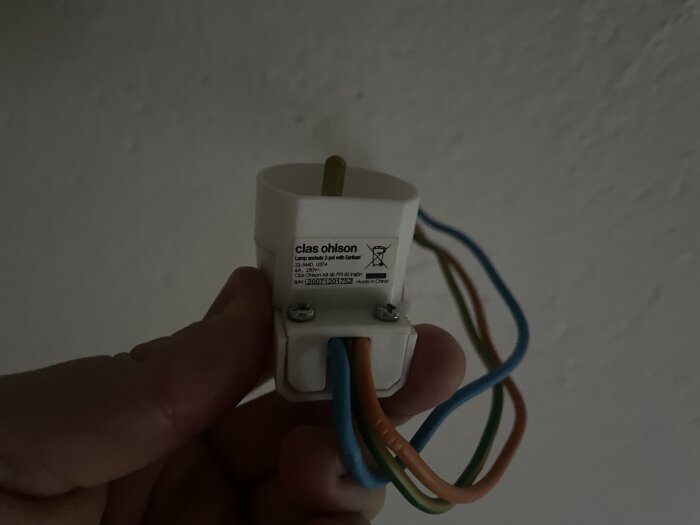 Hand som håller en lamppropp med flerfärgade ledningar, etikett från Clas Ohlson synlig.