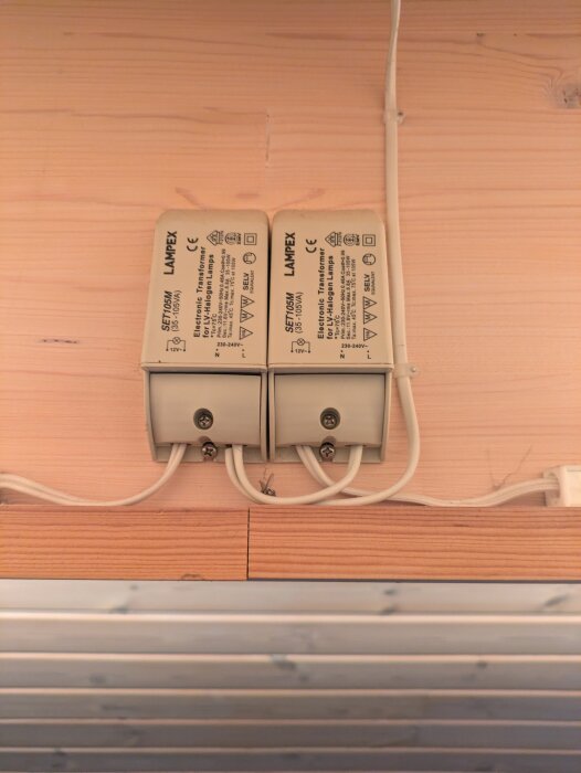 Två elektroniska transformatorer för halogenlampor monterade på limträbalk vid innertaket, med kablar anslutna.