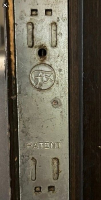 Närbild av en trasig spanjolet där "huset" som innehåller handtagsmekanismen har börjat glida isär, med synliga tappar och texten "PATENT".