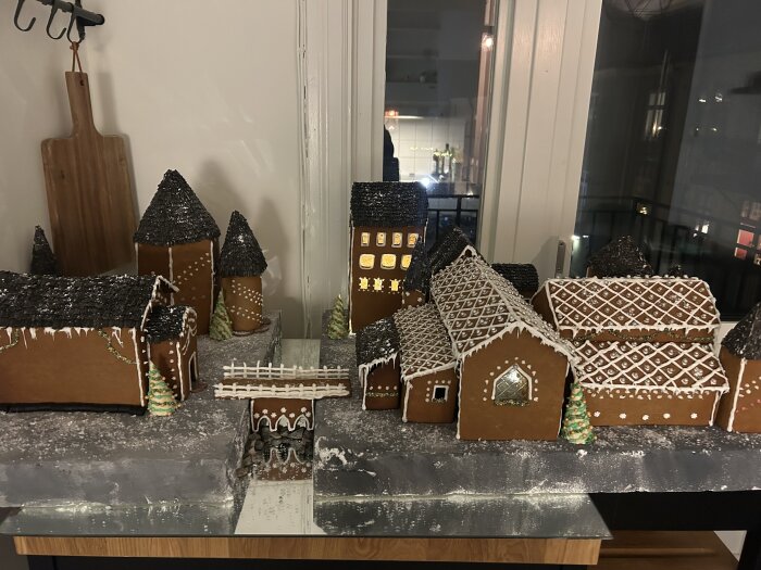 Ett pepparkakshus med flera byggnader dekorerade med kristyr och strössel, upplyst i ett dunkelt rum.