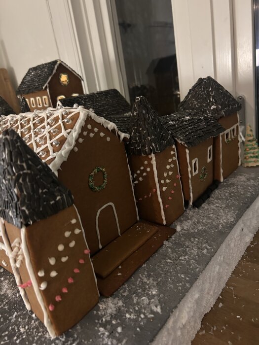 Pepparkakshus med snötäckta tak och dekorationer av glasyr och godis, stående på en snöliknande yta.