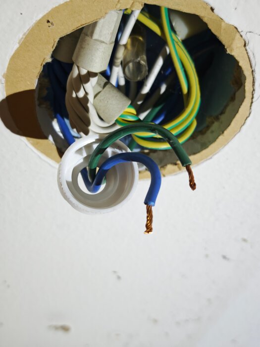 Elektriska kablar och sladdar blottade i ett cirkelformat hål i taket, redo för installation eller reparation.