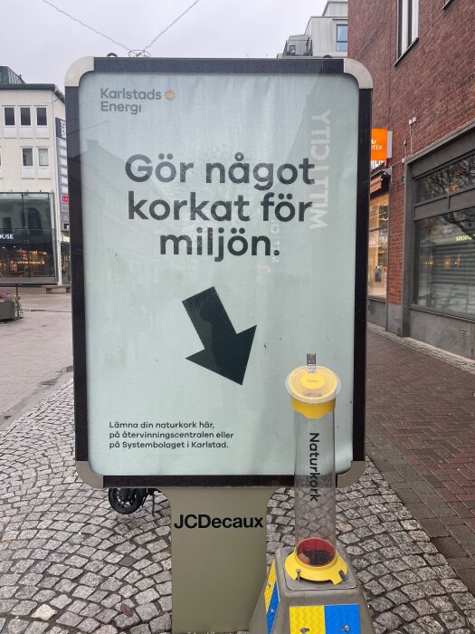 Reklamskylt från Karlstads Energi som uppmanar till att lämna in naturkorkar för återvinning, med en behållare för korkar nedanför.
