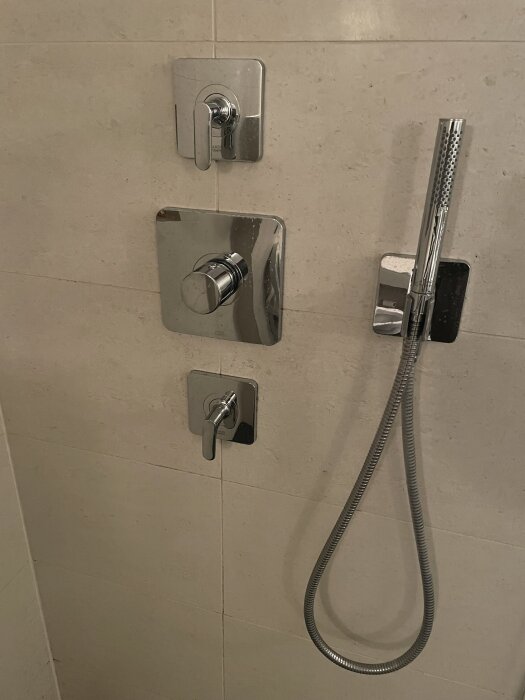 Handdusch och blandare monterade på kakelvägg, fokus på droppande munstycke och diskussion om termostatfel.