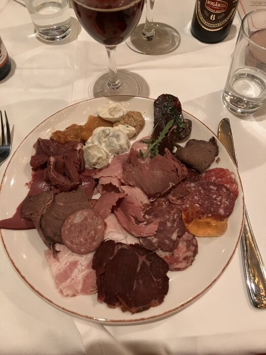 Julbordstallrik med olika köttsorter och såser, serverad med ett glas rött öl.