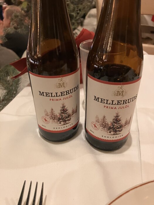 Två flaskor Melleruds Prima Julöl på ett julbord, omgivna av juldekorationer.