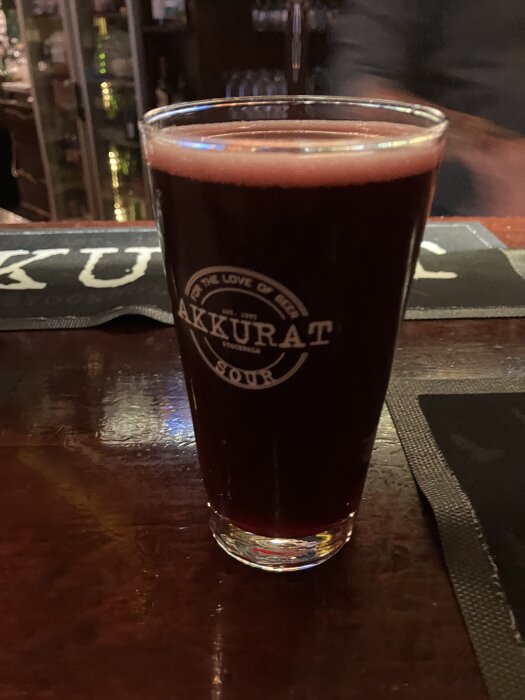 Ett glas rödbrun öl med "Akkurat Sour" logo på barbord, del av ett julbordsevent.