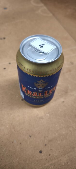 Burk öl av märket Král Lev med etiketten nummer 4 placerad på locket, står på ett bord.