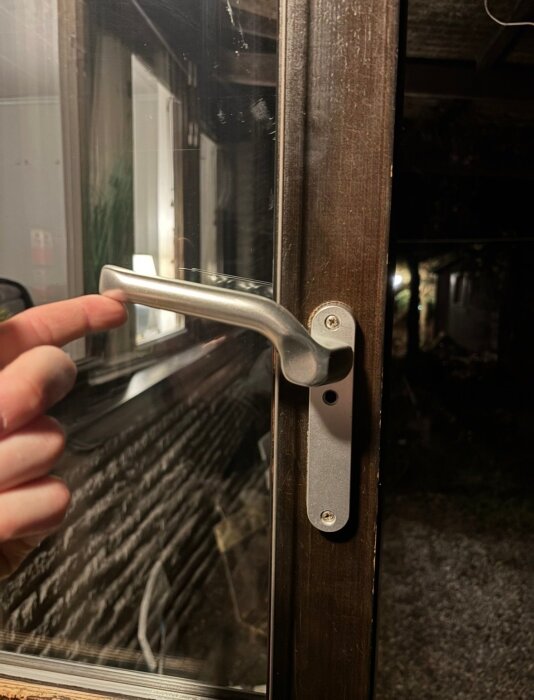 Handtag på ett fönster eller en dörr visas i öppet läge, med en hand som pekar mot handtaget mot en mörk bakgrund.