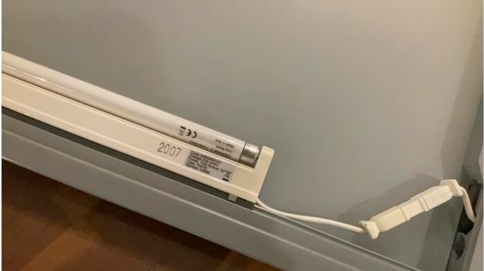 Trasig armatur med T5-lysrör placerad på en köksbänk. Modellnummer och en elkabel syns tydligt.