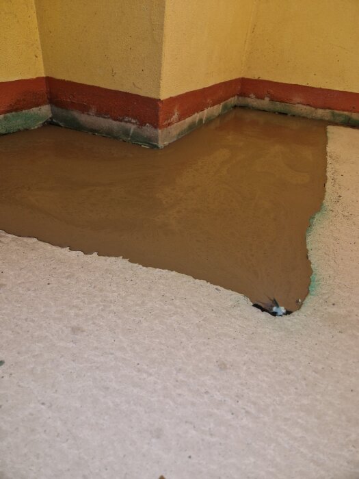 Betonglagning på golv i ett hörn, med jämn och nylagd yta, omgiven av gula och röda väggar samt grönt inslag vid kanten.