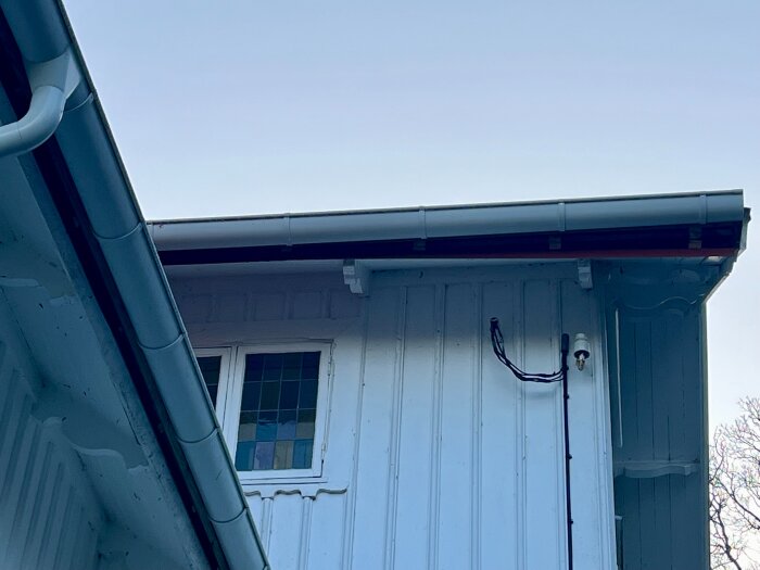 Husfasad med nyinstallerat tak, hängränna och synliga läkt under rännan, uppvisar potentiell byggdetalj för bedömning.