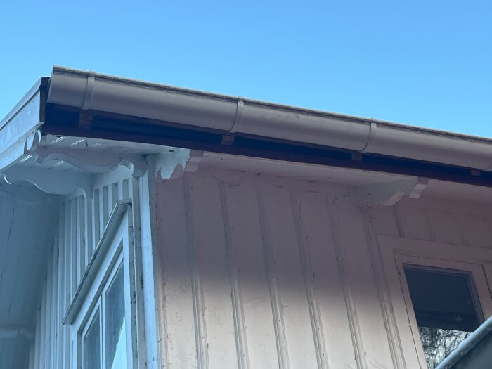 Takfot och stupränna på ett vitt trähus mot en klarblå himmel.